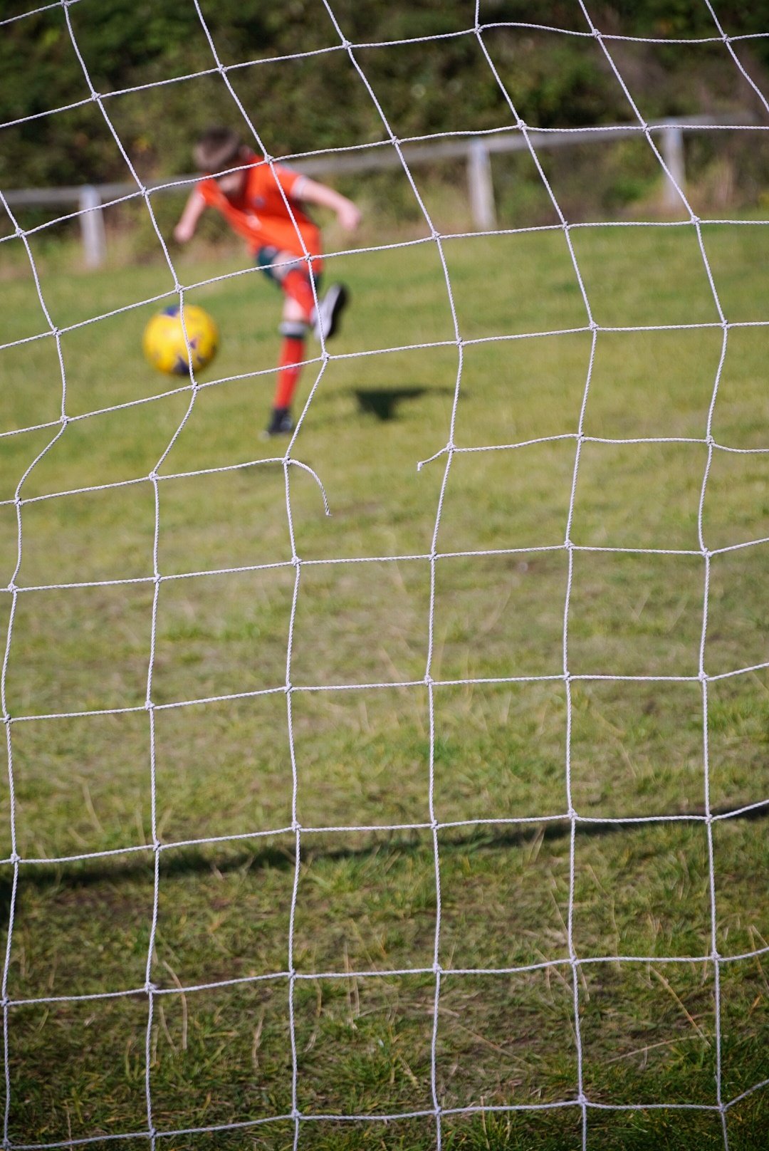 Child playing football, photographed through the goal net