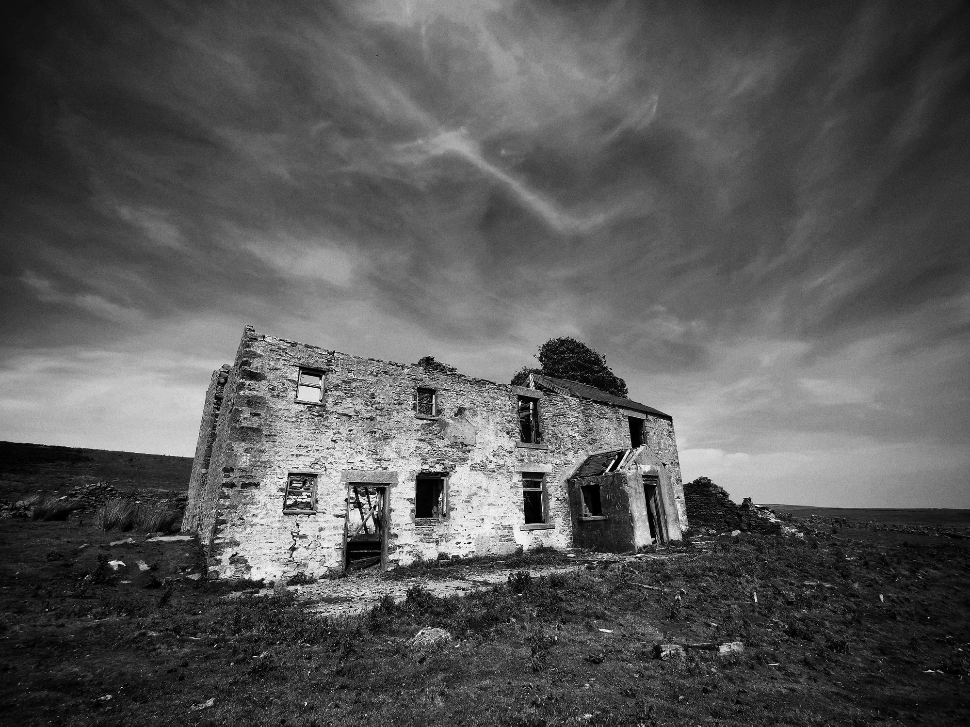 Derelict stone farmhouse on open moorland under a dramatic cloudy sky