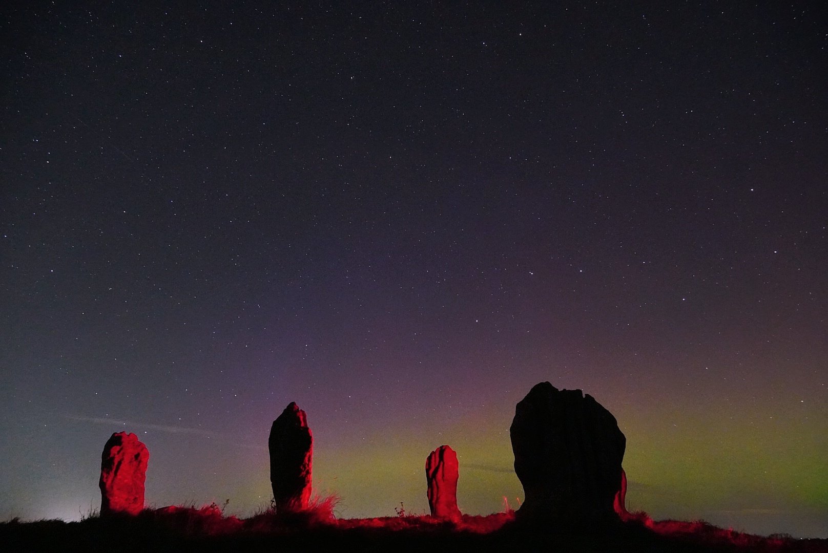 Duddo Standing stones lit red at night beneath the northern lights
