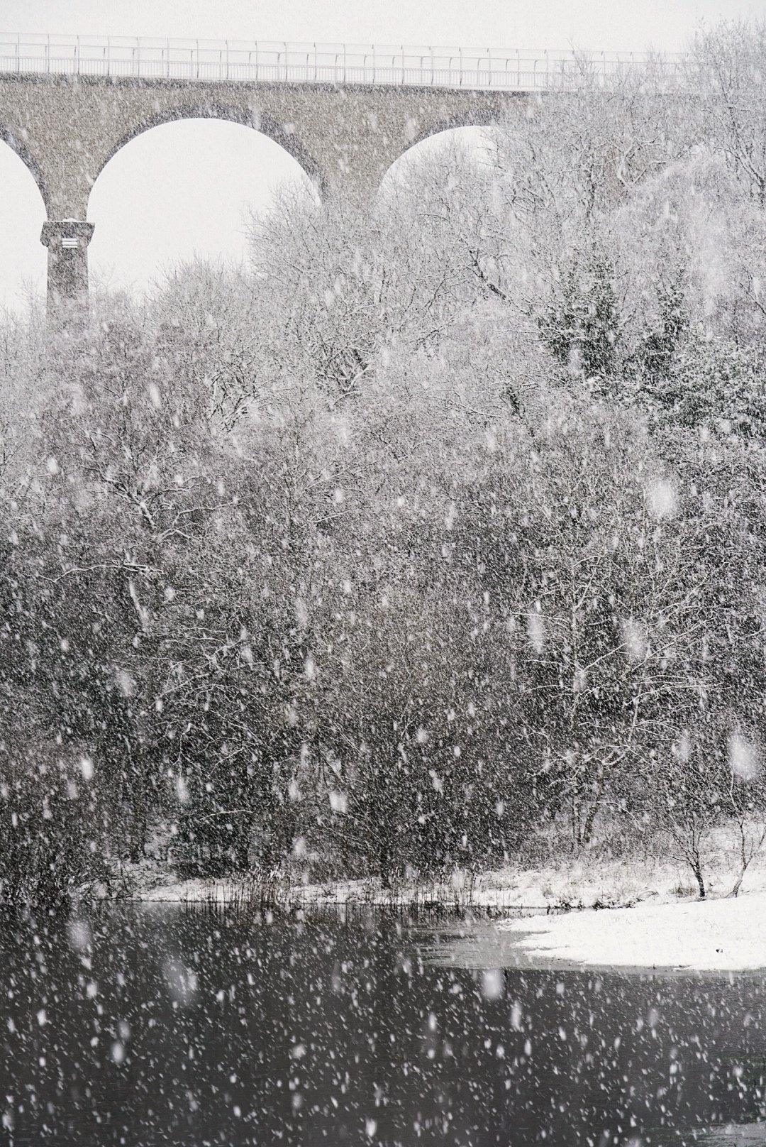 Railway viaduct in heavy snowfall with a river below